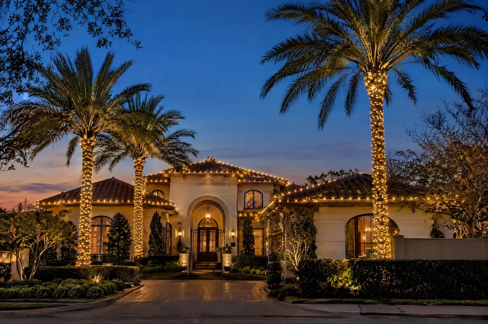 Mediterranean home with a tile roof, lit arches, and palm trees wrapped in warm white lights