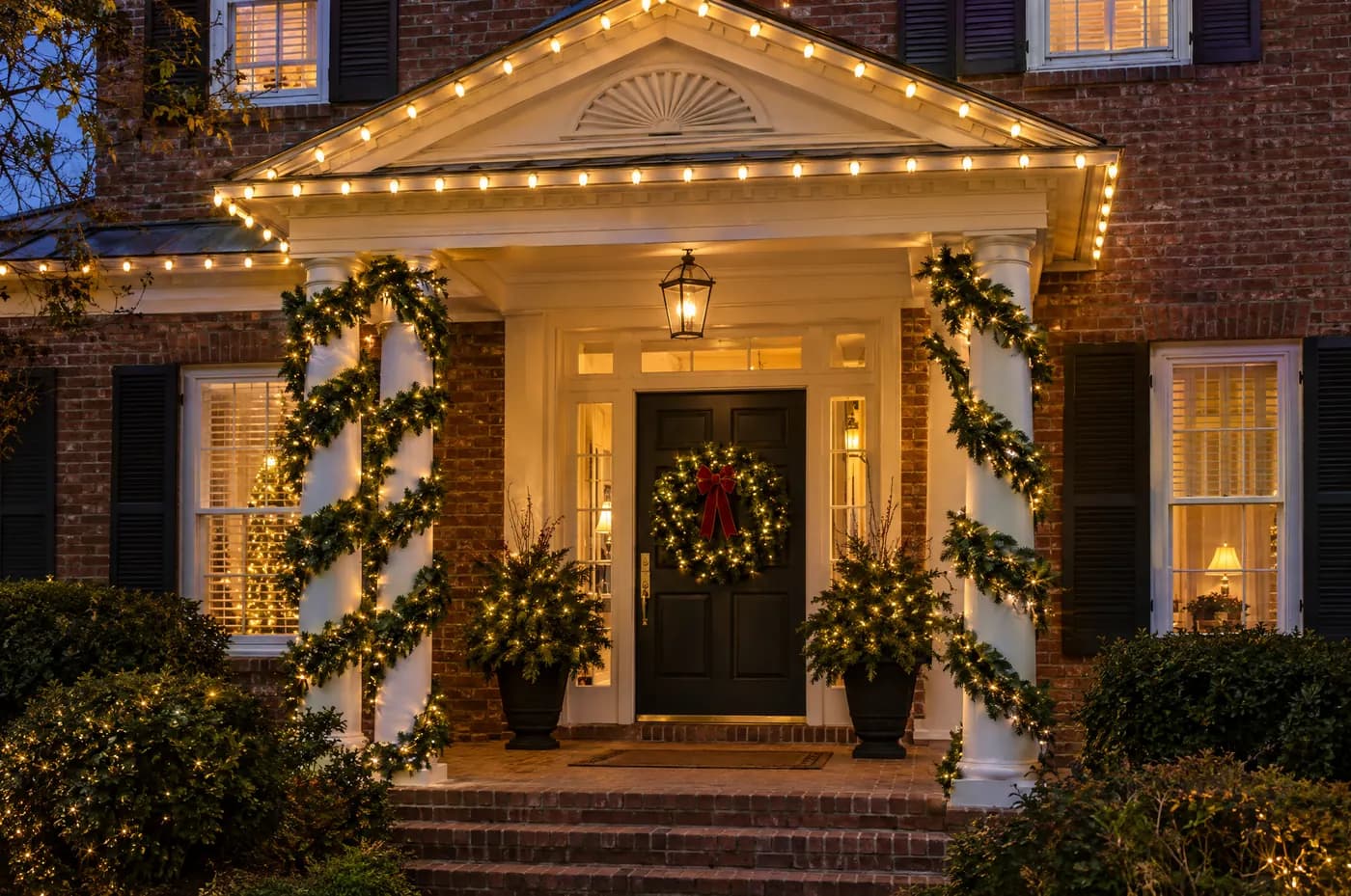 Front portico with a lit pediment and columns wrapped in garland and warm white lights